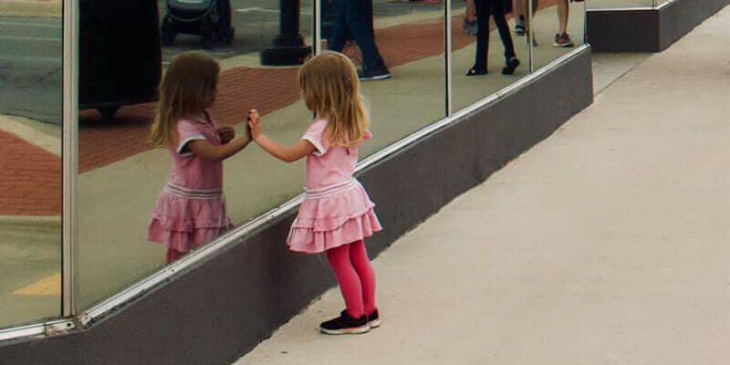 A little girl looking at her reflection in glass at Art and Stroll