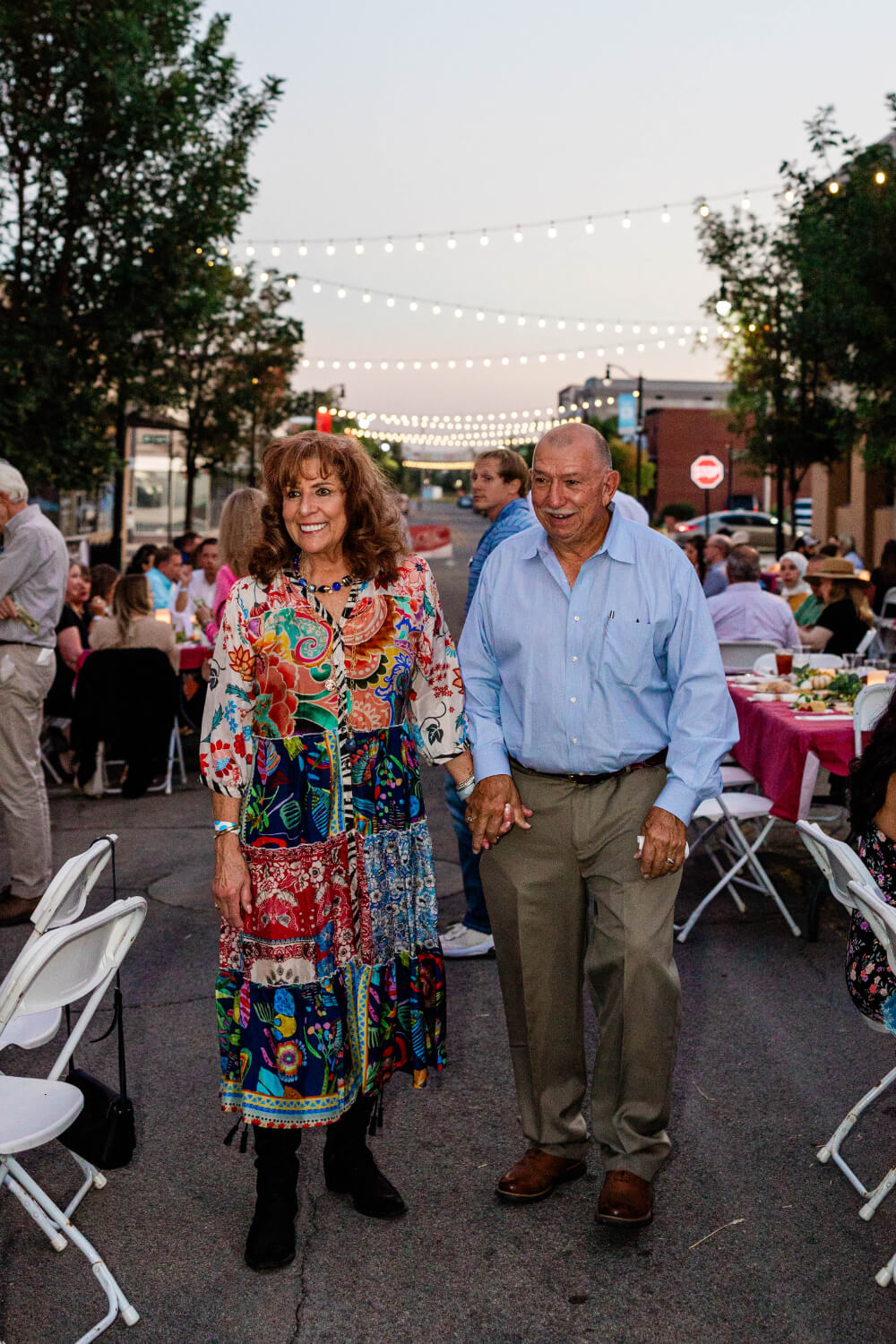 A man and woman walking between outdoor dining tables beneath the string lights.