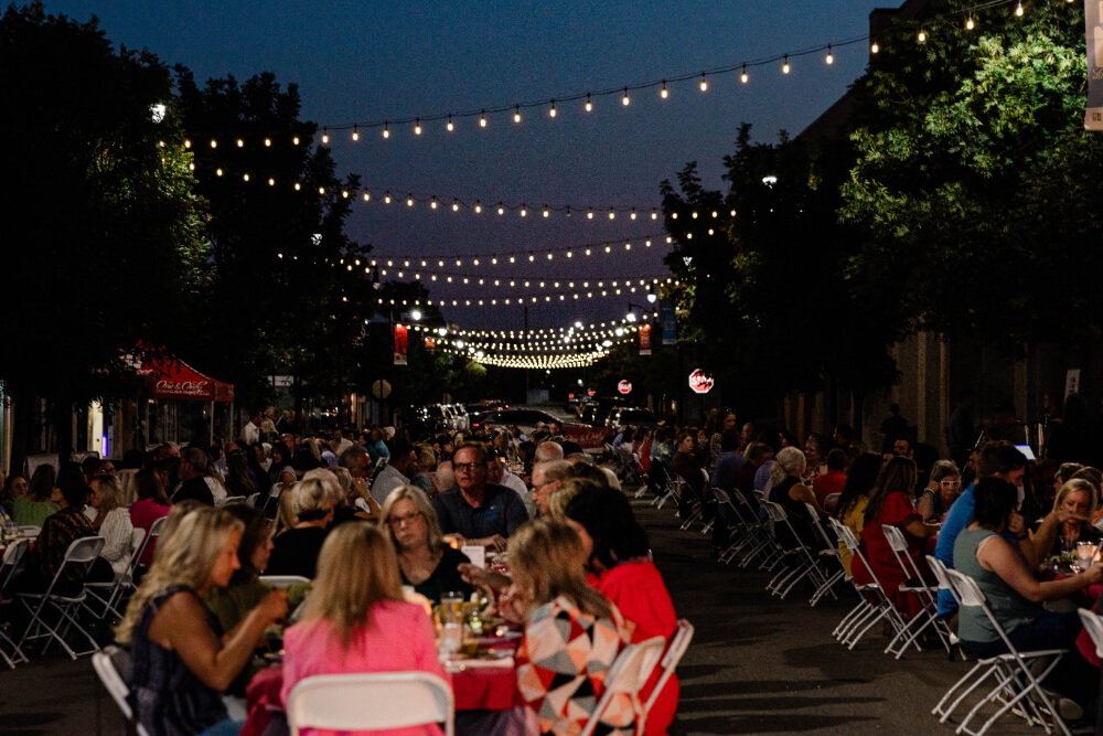 A large crowd dining on Pruett Street beneath glowing string lights at night.